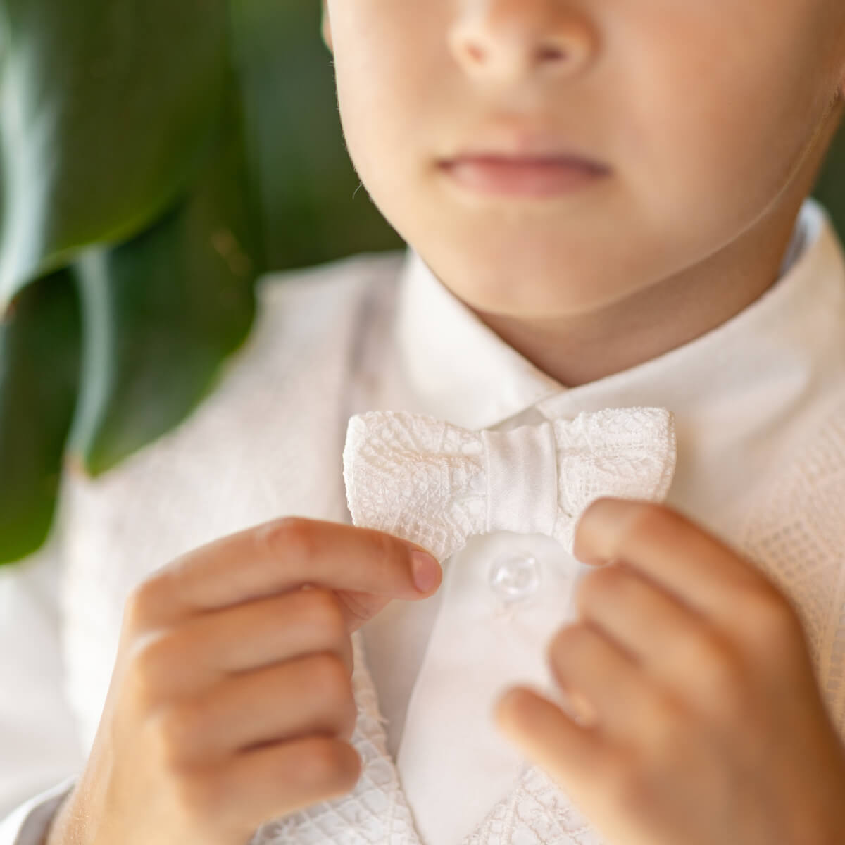 Child wearing a white lace bow tie with a blurred green leaf background