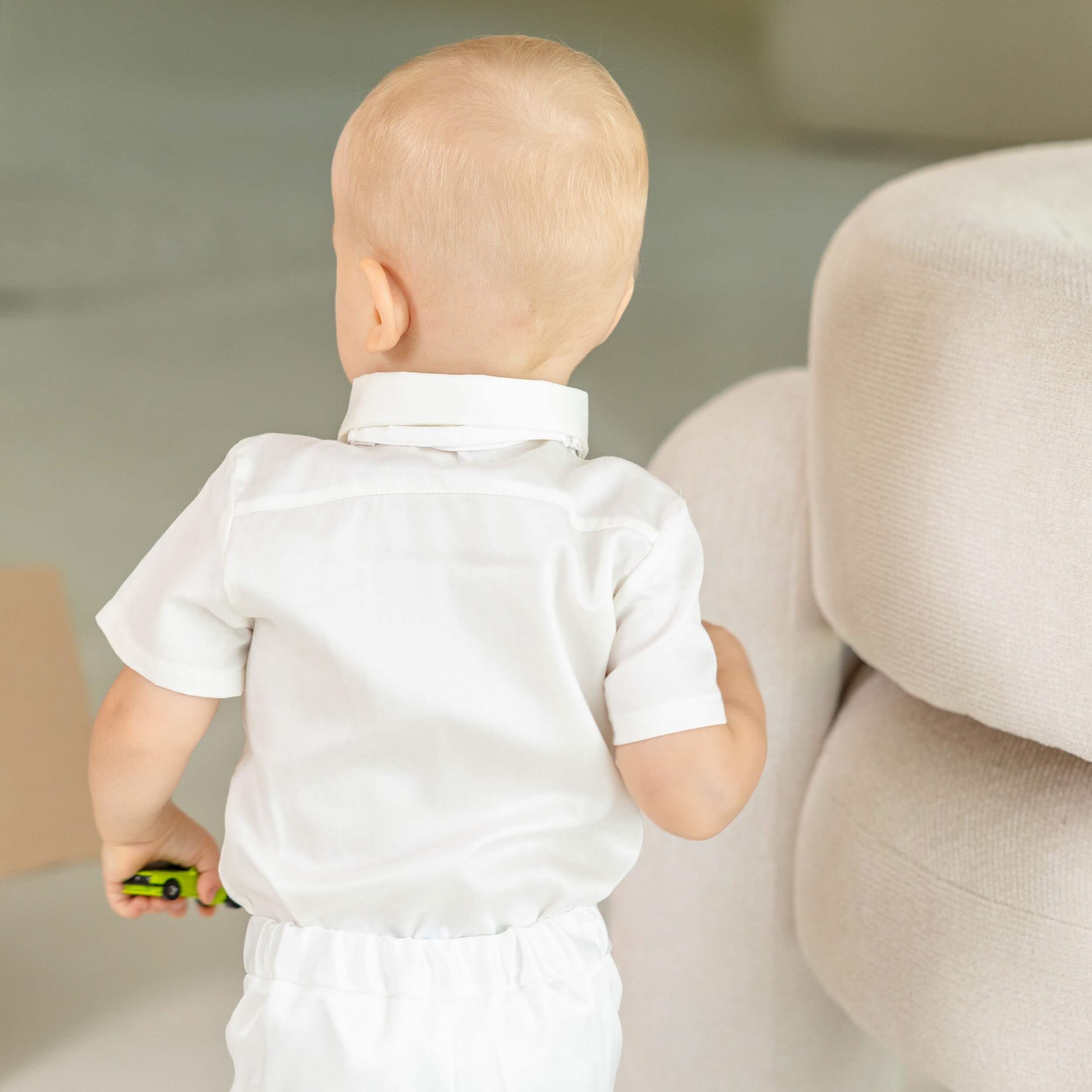 Baby in a Baby Boy Baptism Suit standing near a beige couch