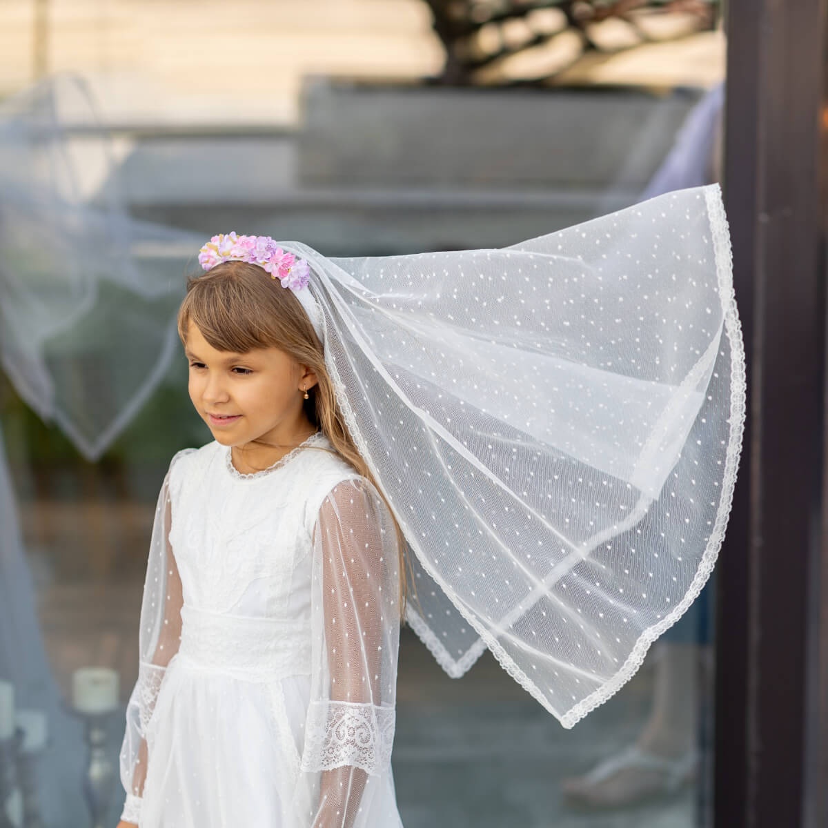 Young girl in a white Traditional Communion Dress with a veil outdoors