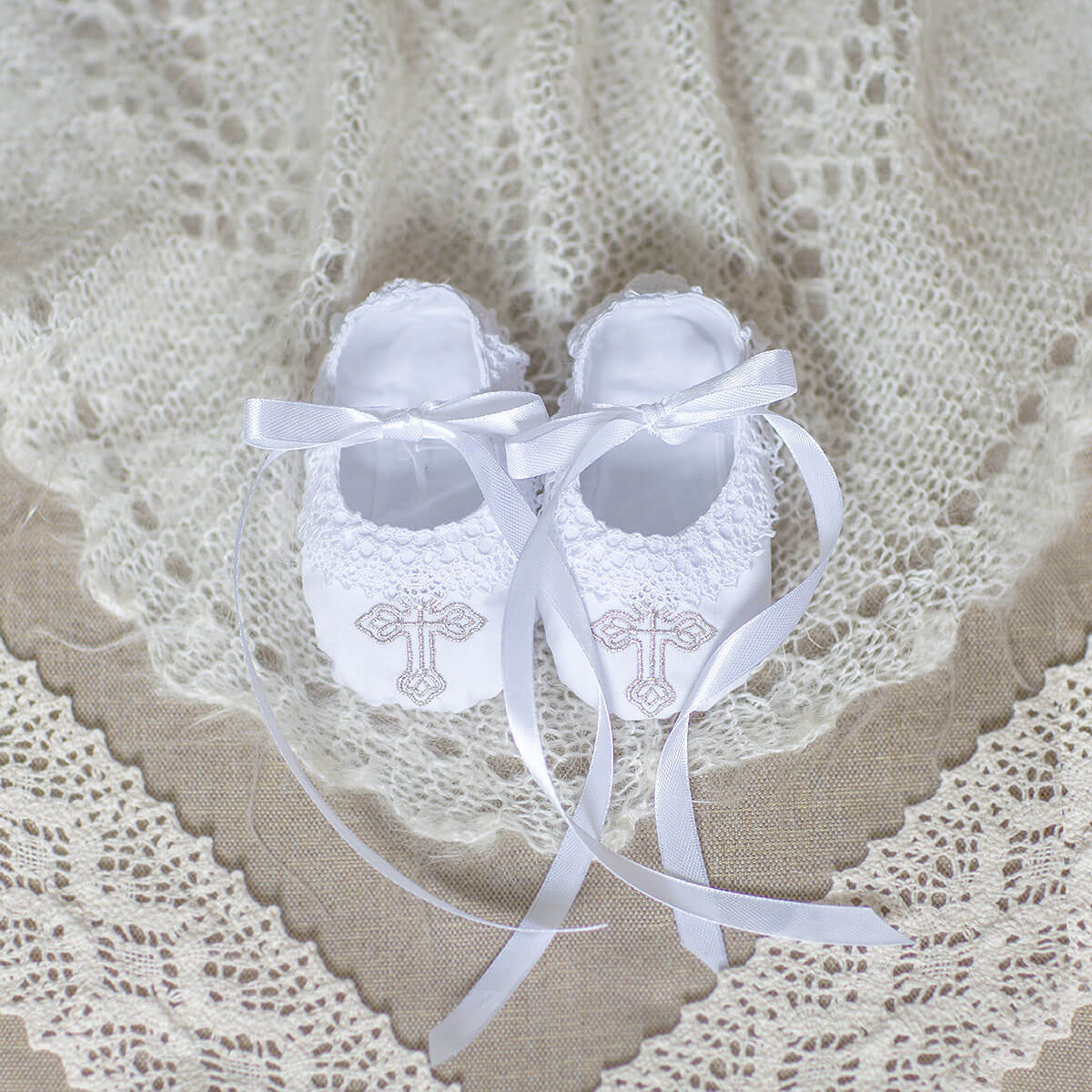 Christening Booties with ribbons on a lace background
