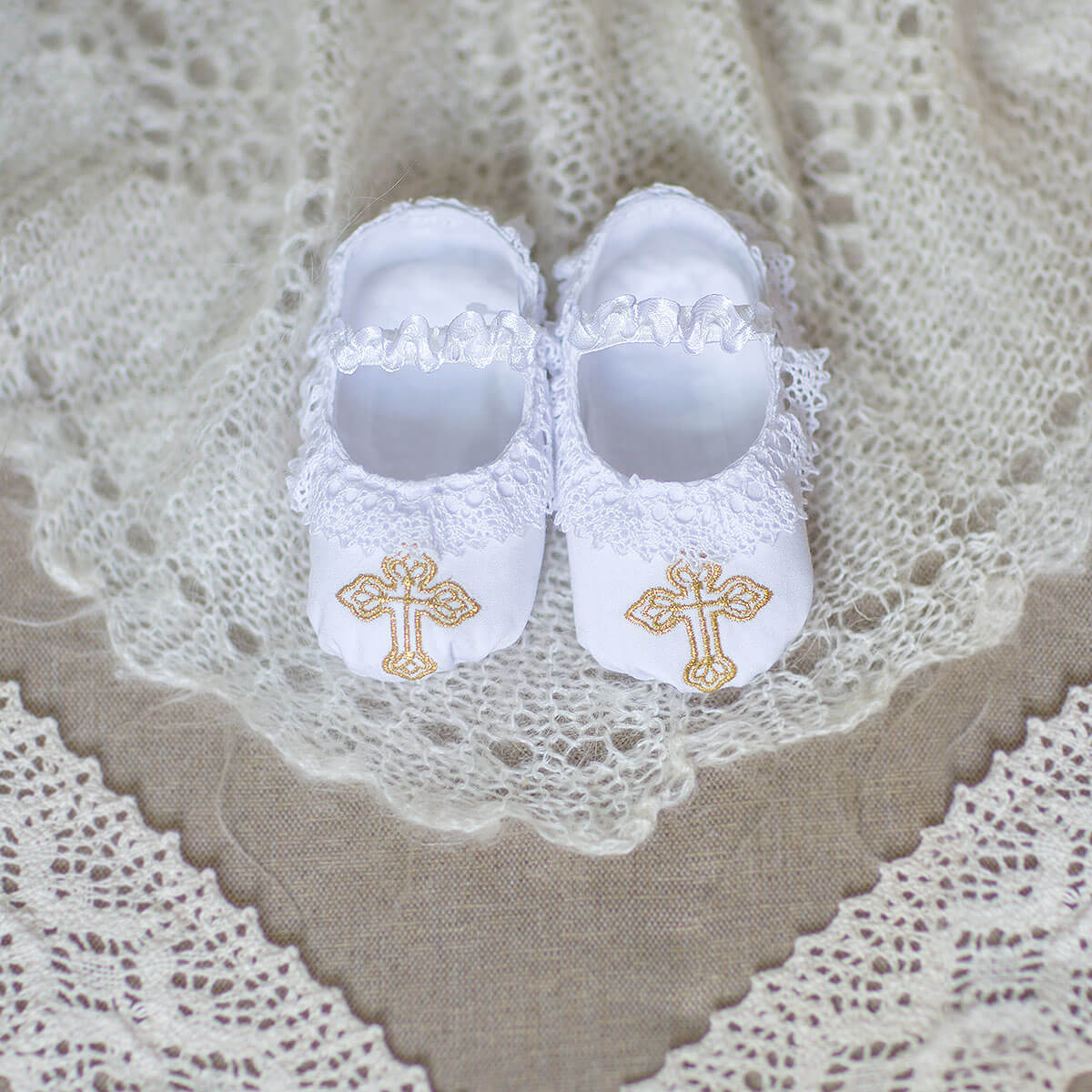 Christening Booties with gold crosses on a lace background
