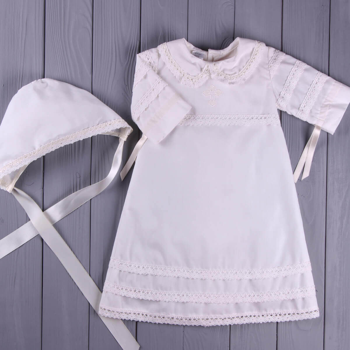 Baptism Gown for Boy with lace details and matching bonnet on a wooden surface