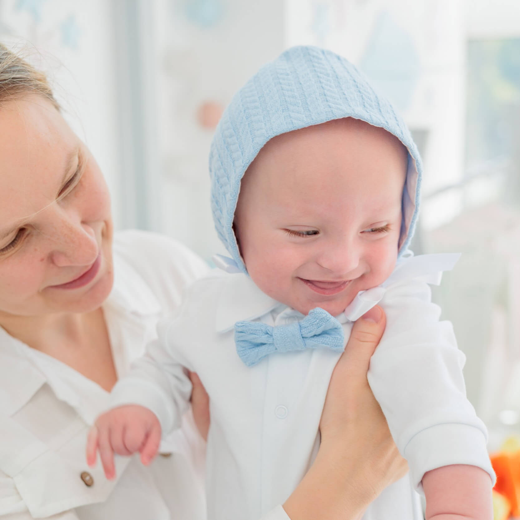 Woman holding a baby wearing a blue bonnet and Newborn Coming Home Outfit in a bright setting