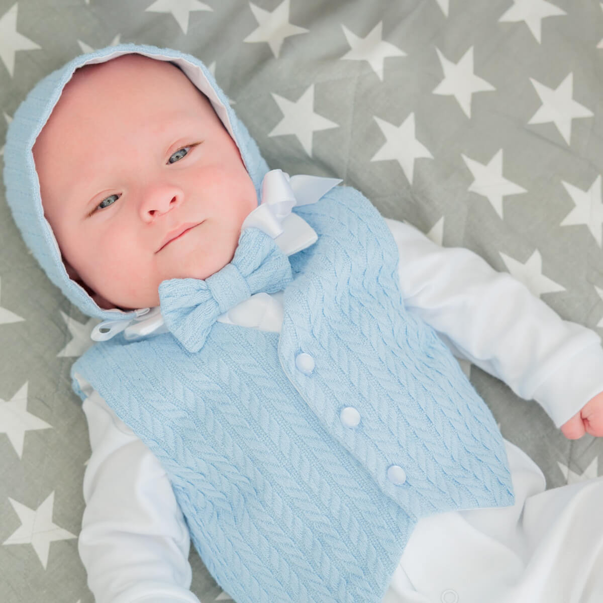 Baby wearing a lNewborn Coming Home Outfit with a hood on a gray blanket with white stars.