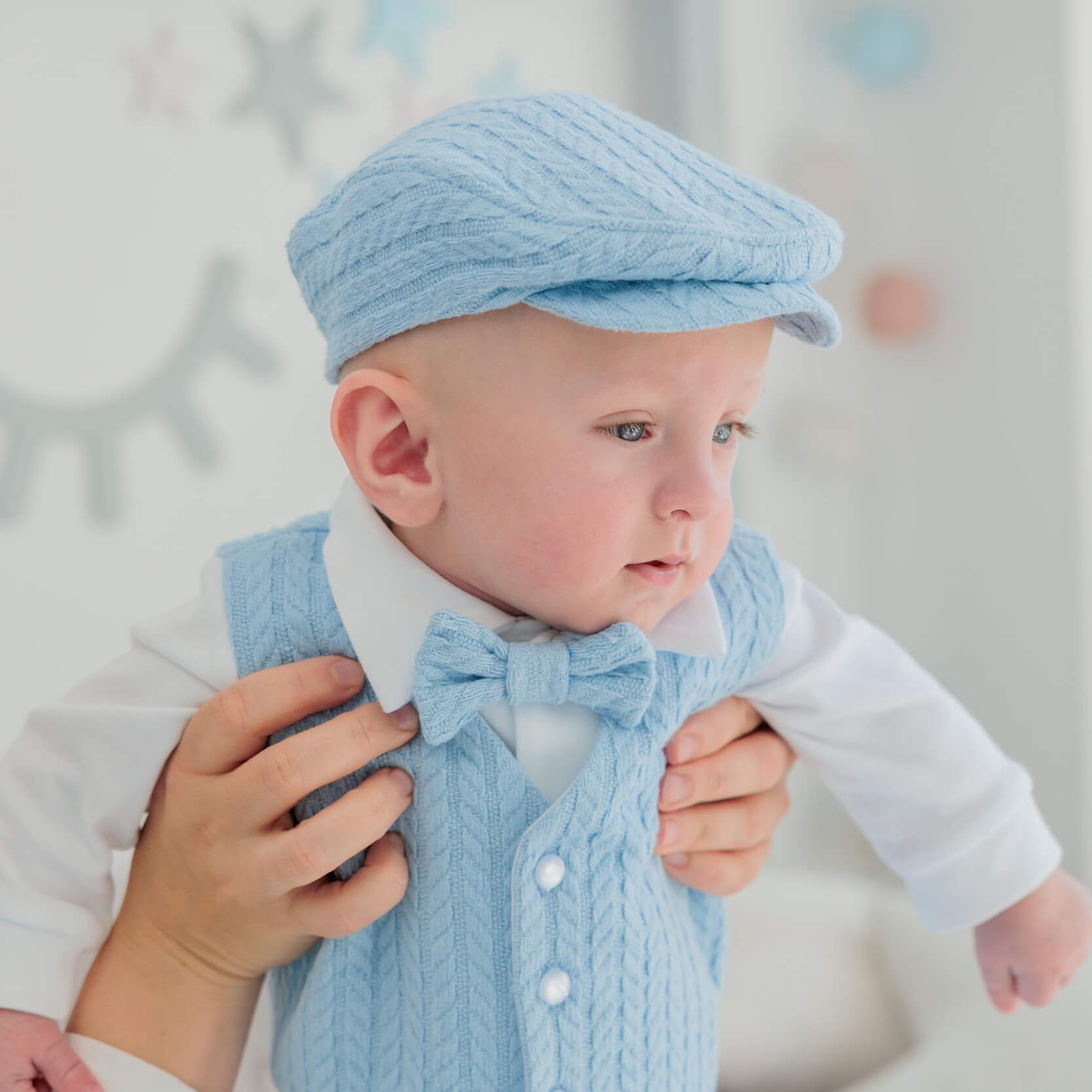 Baby wearing a Newborn Coming Home Outfit with a bow tie and cap, held by an adult.
