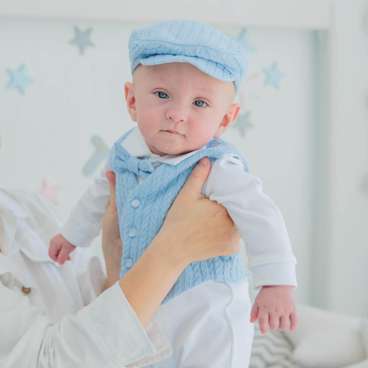 Baby in Newborn Coming Home Outfit and hat being held in a nursery with white walls and star decorations.