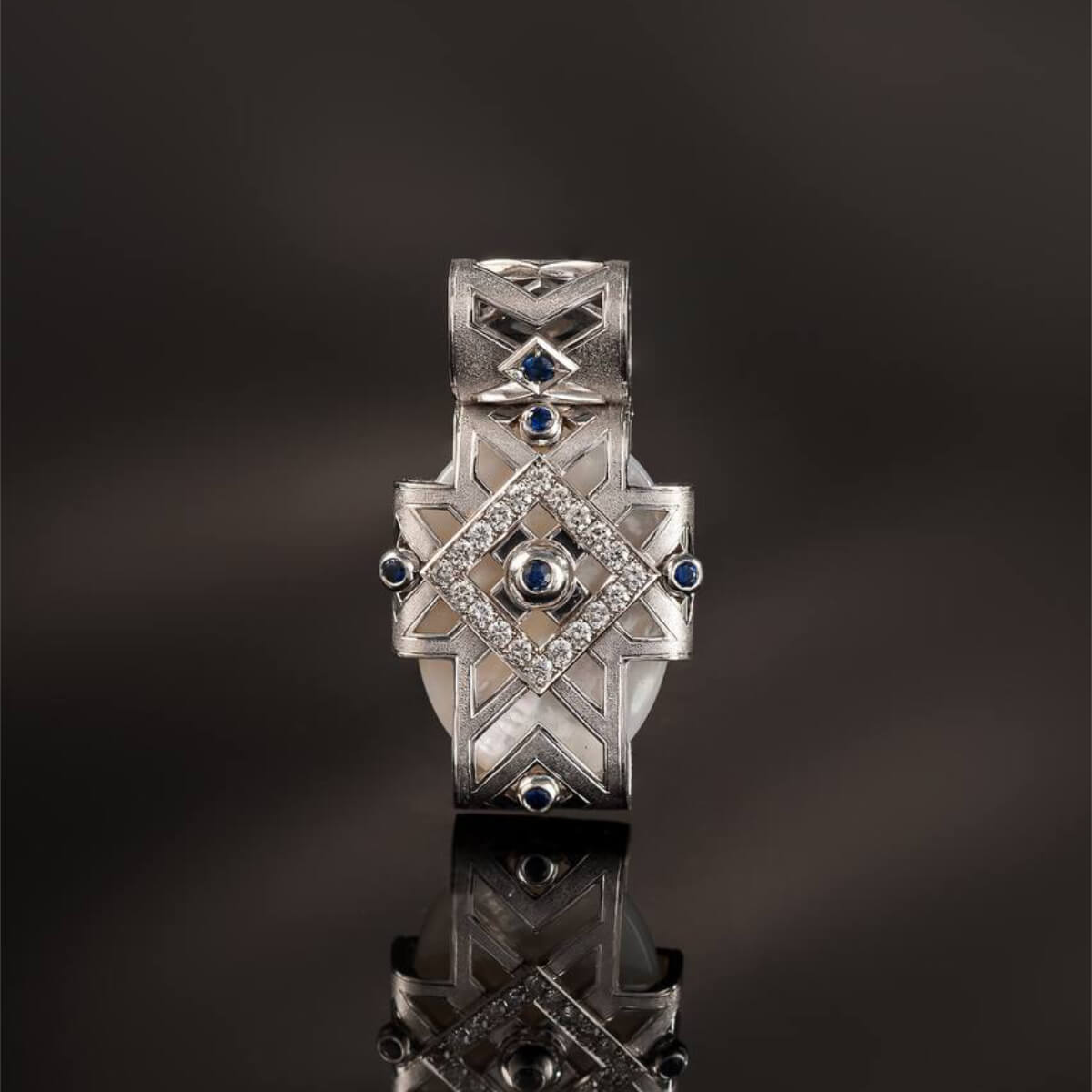 Silver ring with blue gemstones on a reflective surface