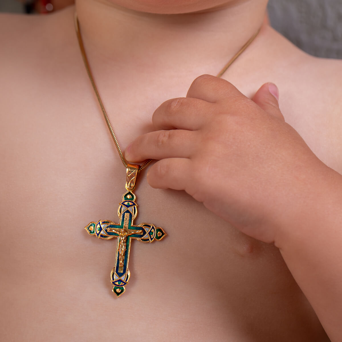 Child's hand touching a gold Classic Baptism Gold Cross – Handcrafted Crucifix Pendant