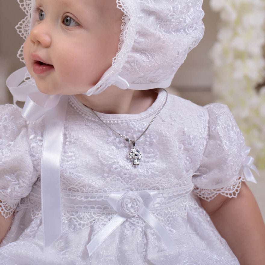 Baby in a white lace dress and bonnet with a blurred floral background