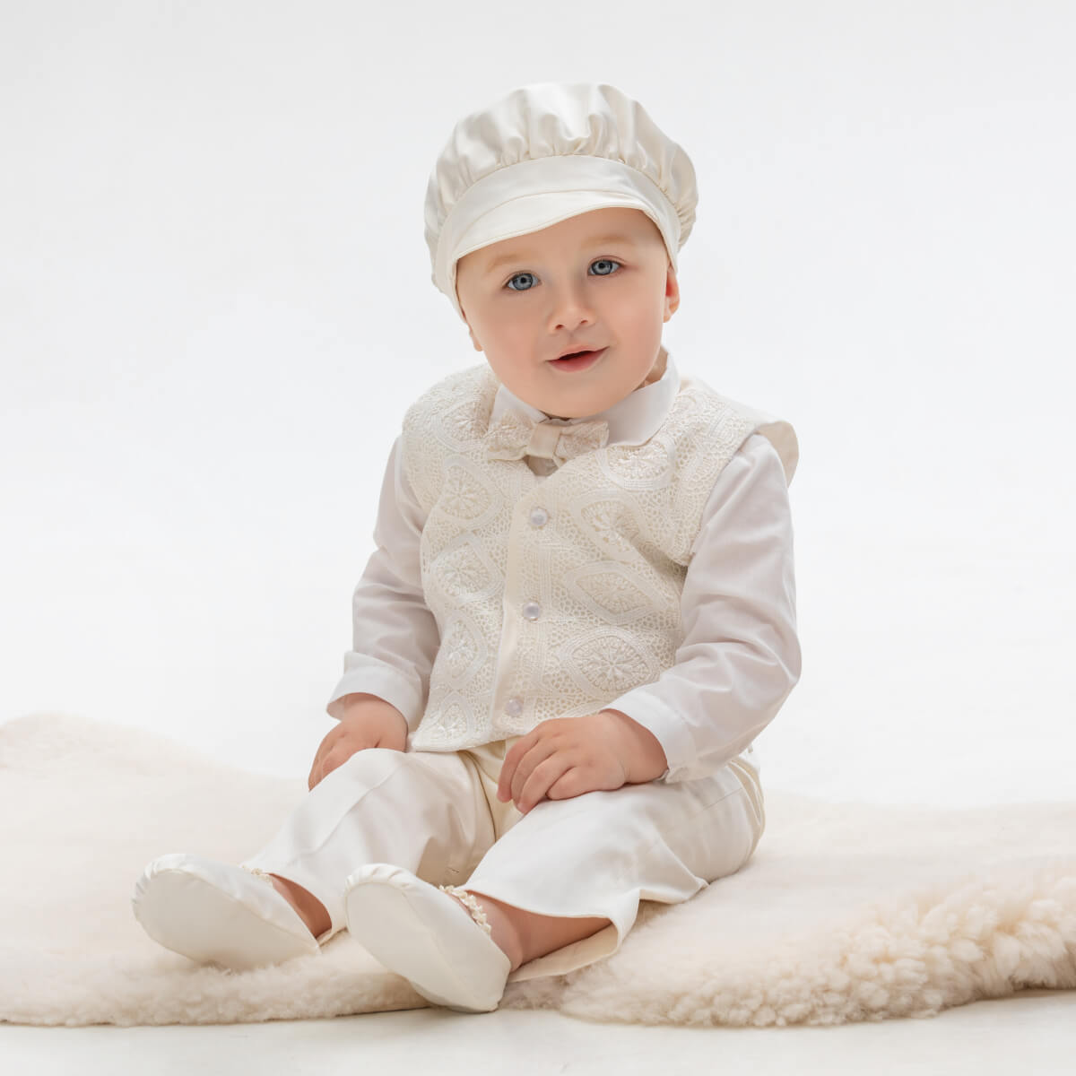 Baby in a  Baby Boy Baptism Suit with a matching hat sitting on a white surface
