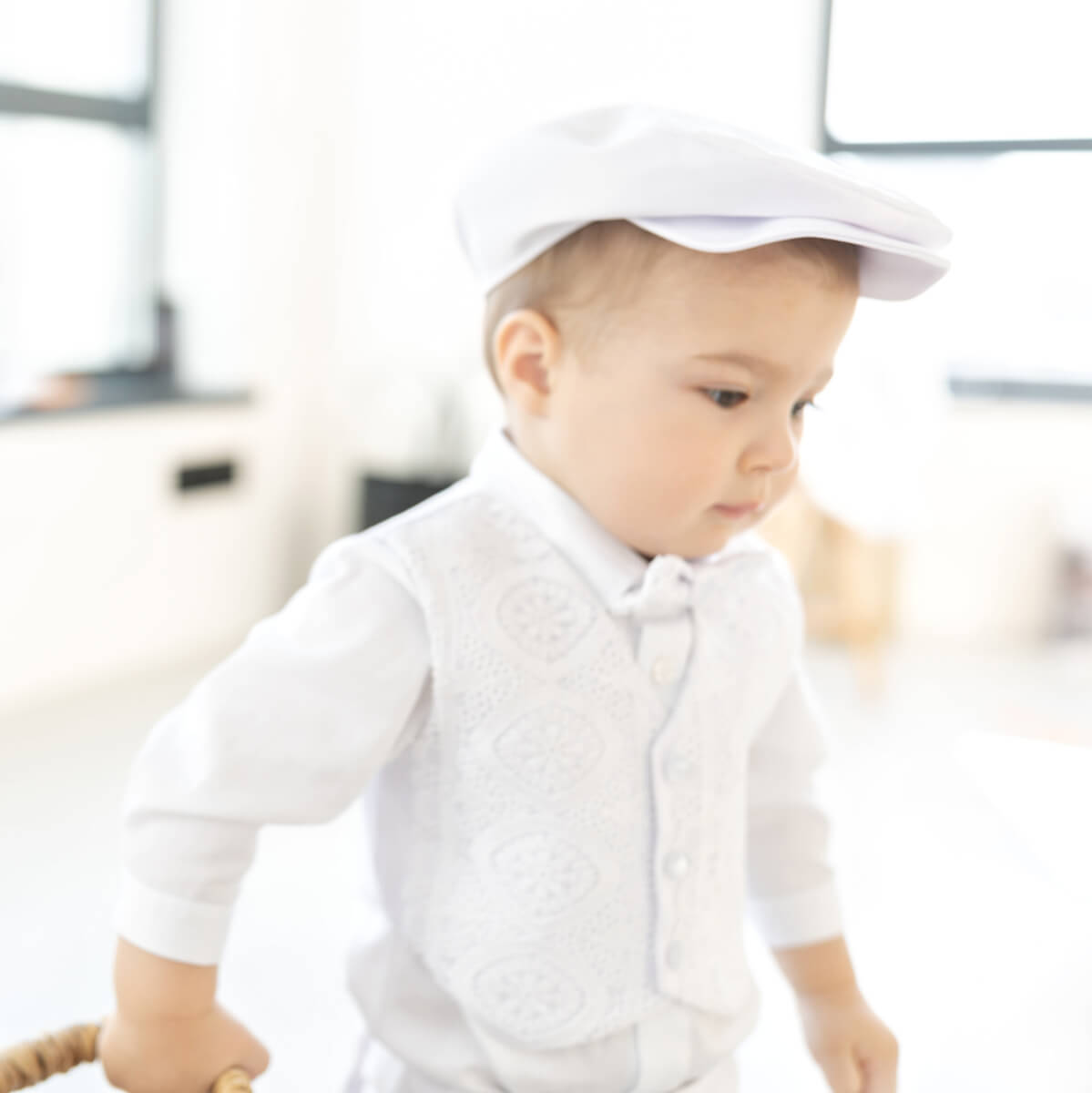 Baby wearing a  Baby Boy Baptism Suit and cap in a blurred indoor setting