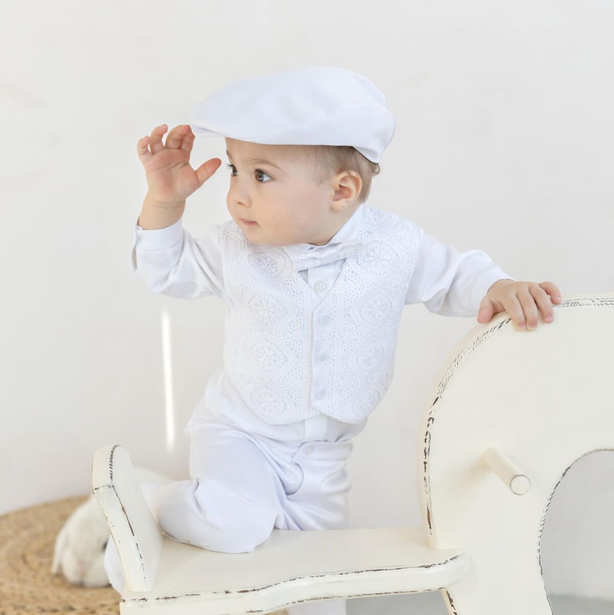 Baby in a  Baby Boy Baptism Suit sitting on a white chair against a plain background