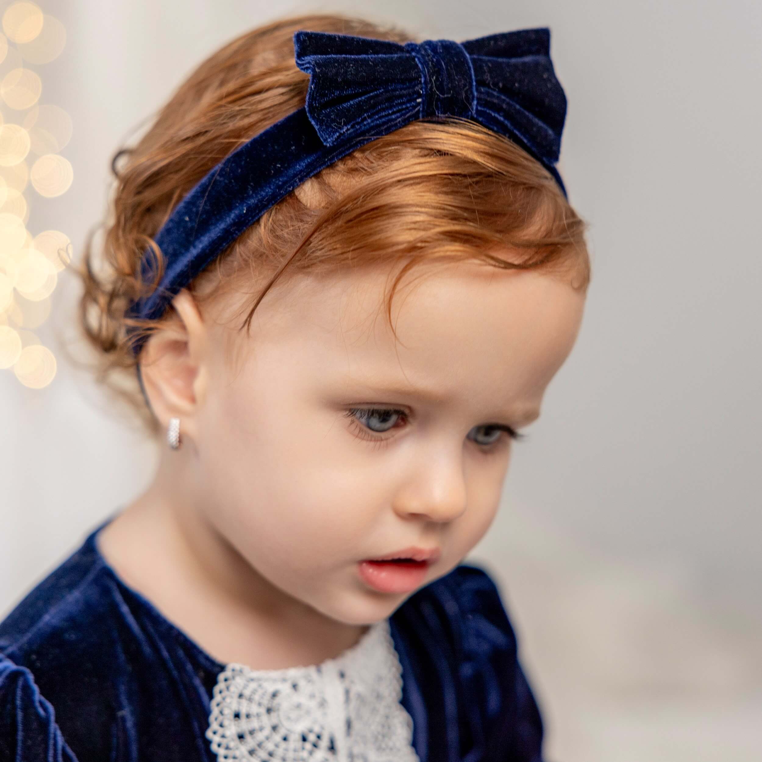 Child wearing a navy blue velvet headband with a bow, against a blurred background.