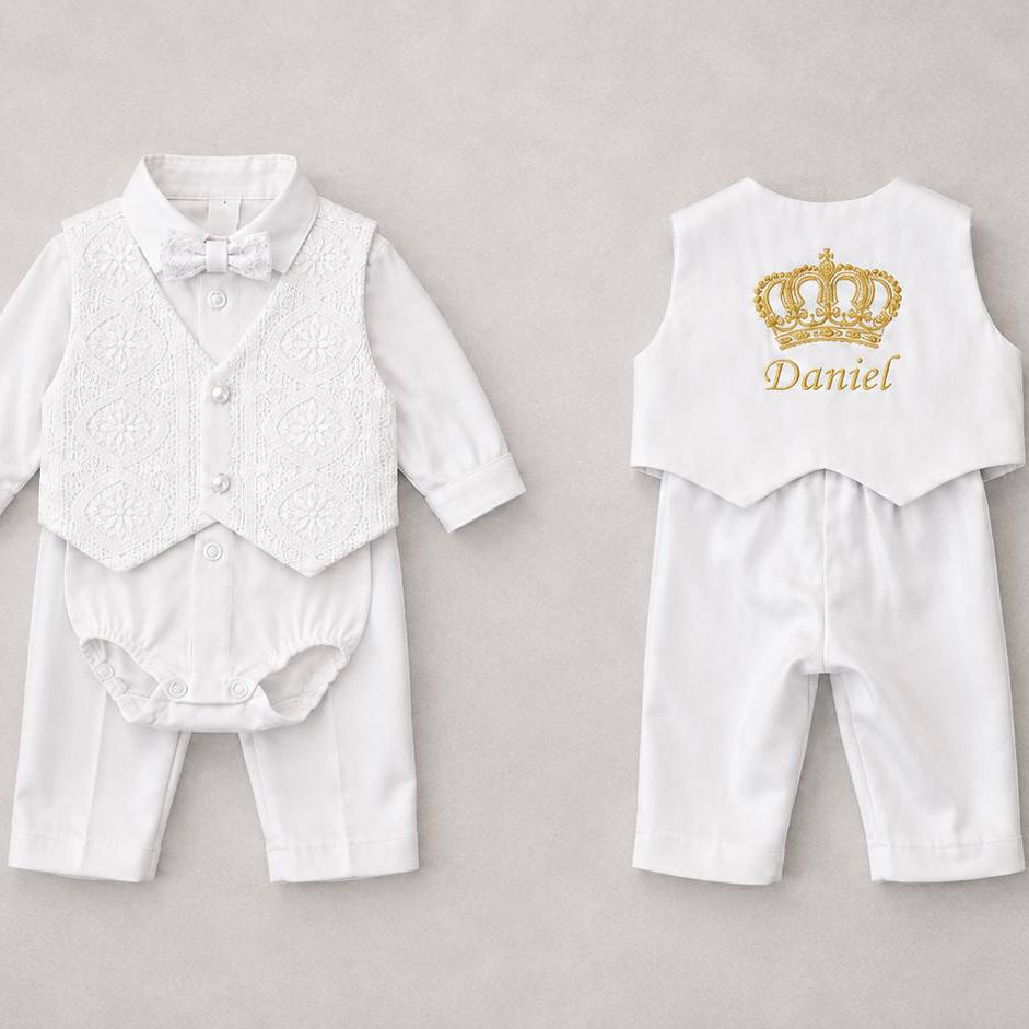 A baby boy's two-piece formal outfit shown from both front and back. The set includes a white long-sleeve shirt with a white textured lace vest and bow tie on the front, and a matching white vest with a gold crown graphic and the name 'Daniel' printed on the back, paired with white pants.