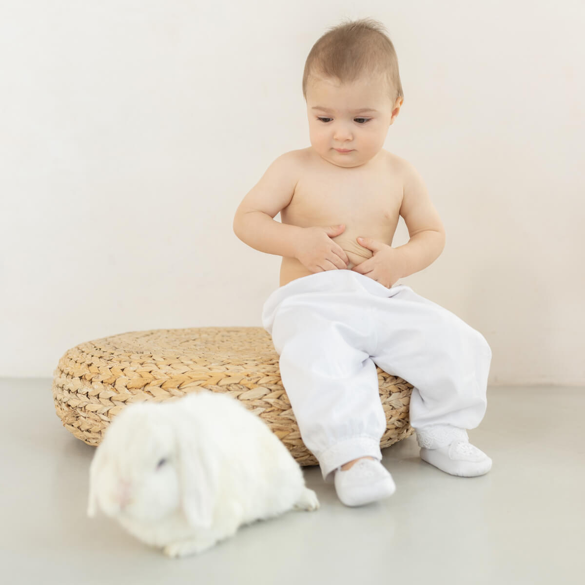 Baby sitting on a woven stool in Baby Boy Christening Suit  on a plain background