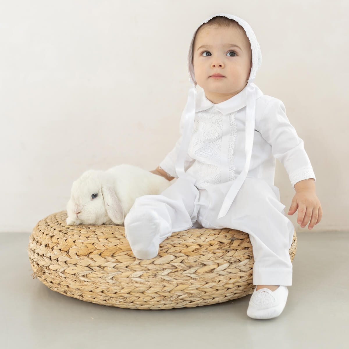 Baby in a Baby Boy Christening Suit  sitting on a woven stool with a white rabbit