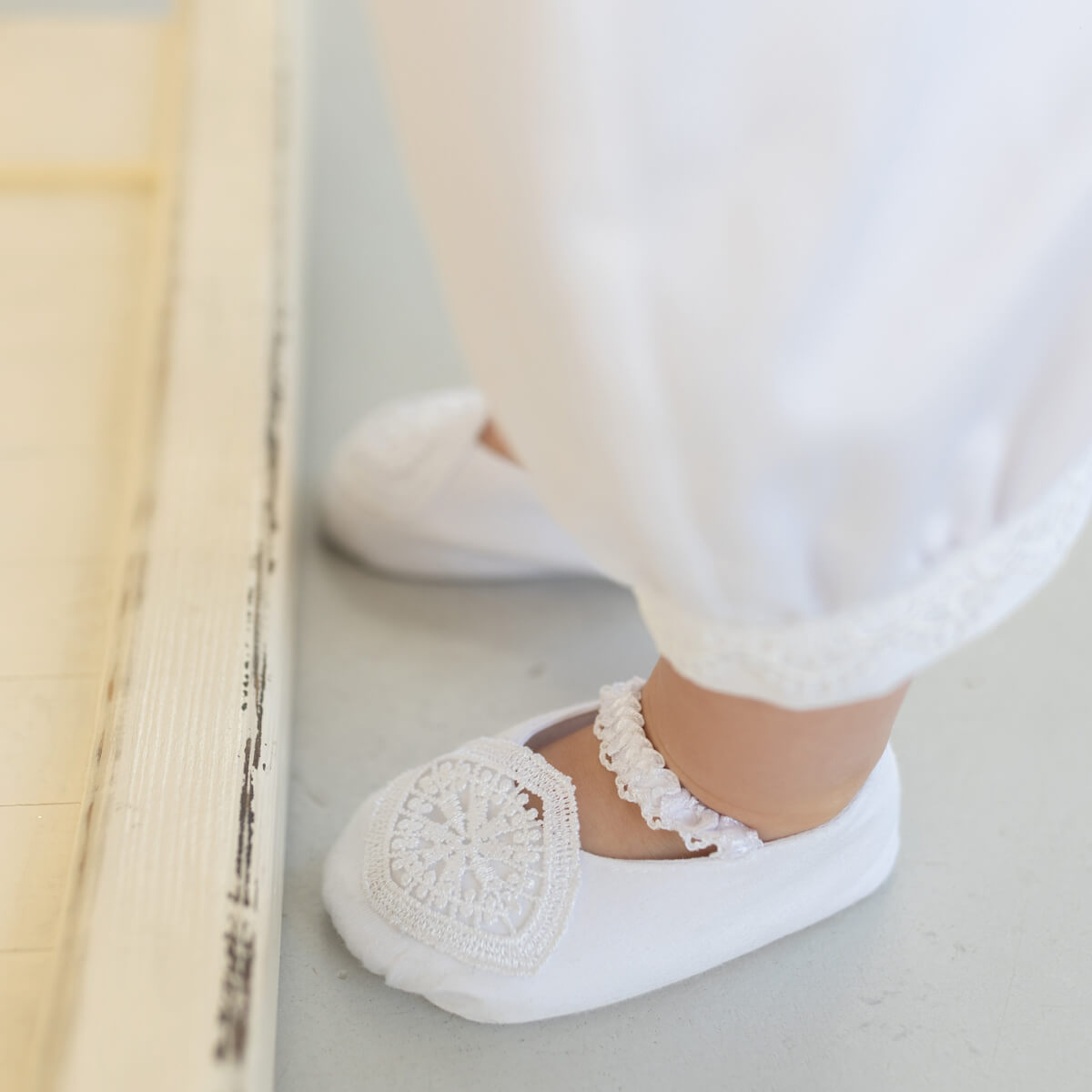   Baptism Booties with lace details worn by a person sitting on a bench.