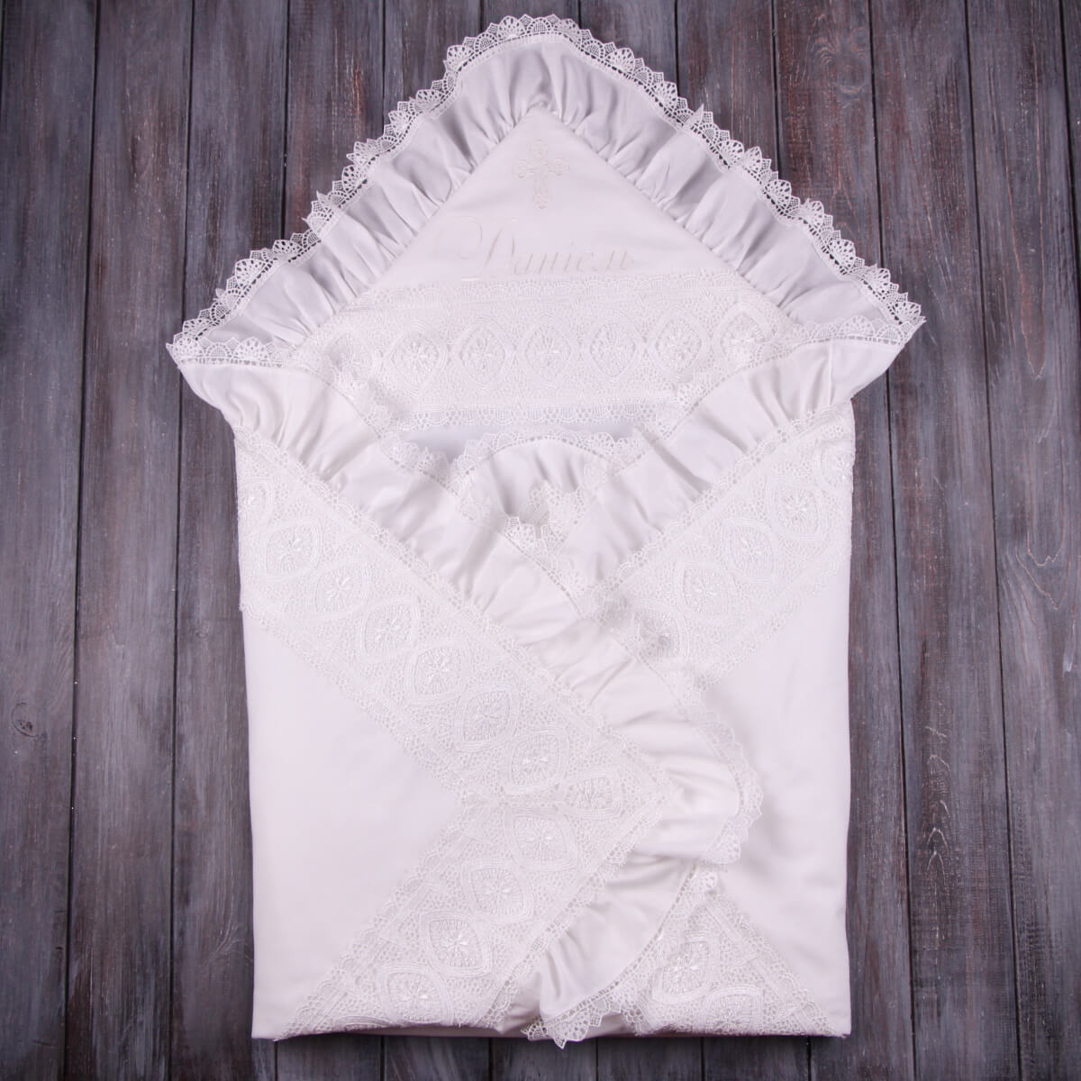 White lace-trimmed baptism blanket on a wooden surface