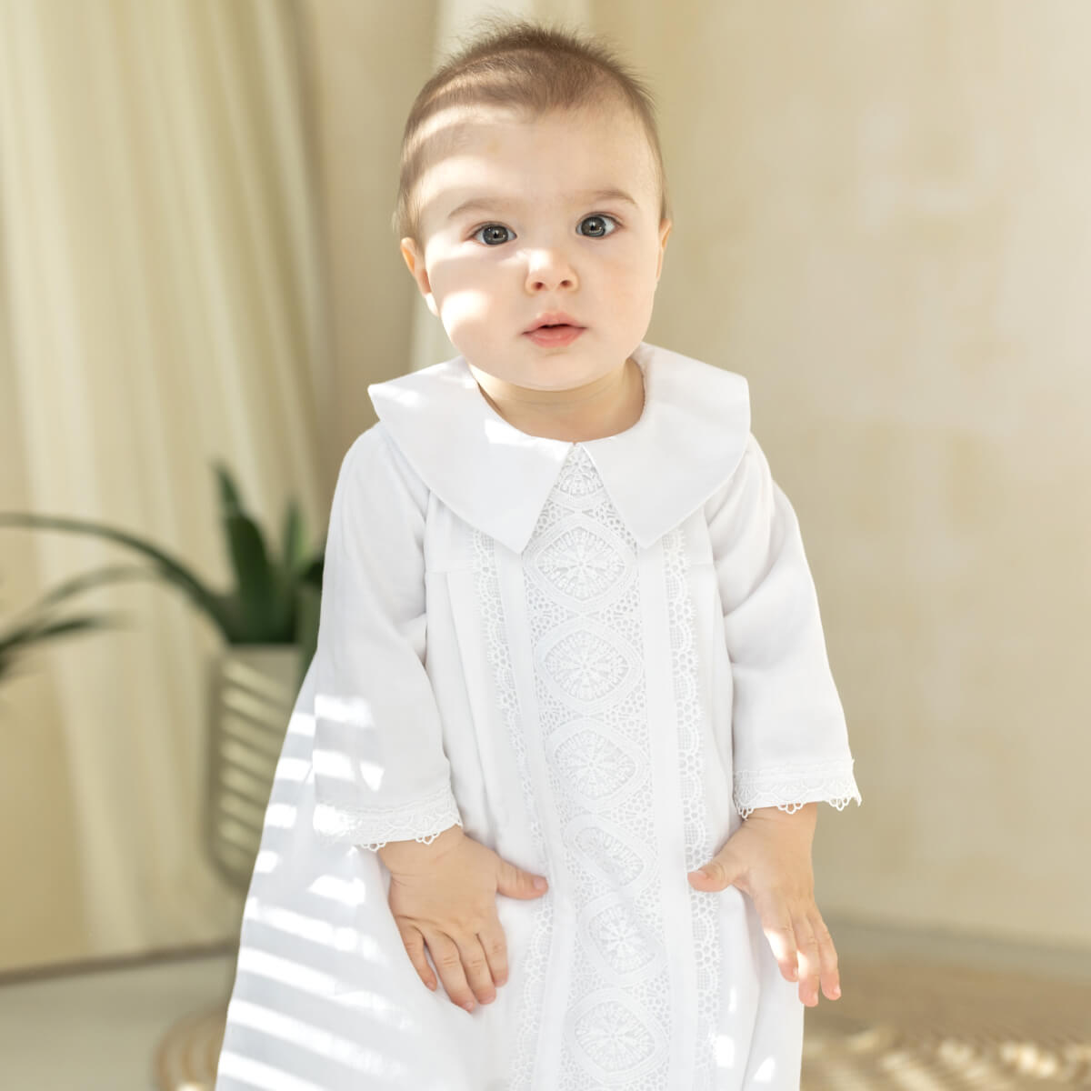 Baby wearing a white christening gown with a collar in a neutral setting