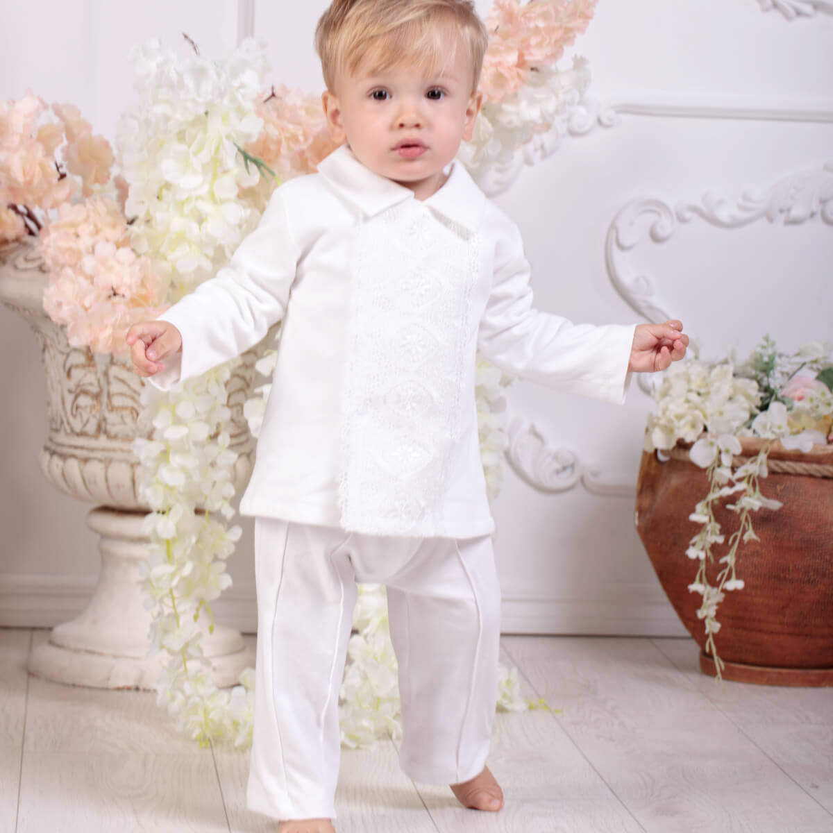 Child wearing a Baby Boy Baptism Jersey Suit  standing in a decorated room with flowers and decorative elements.