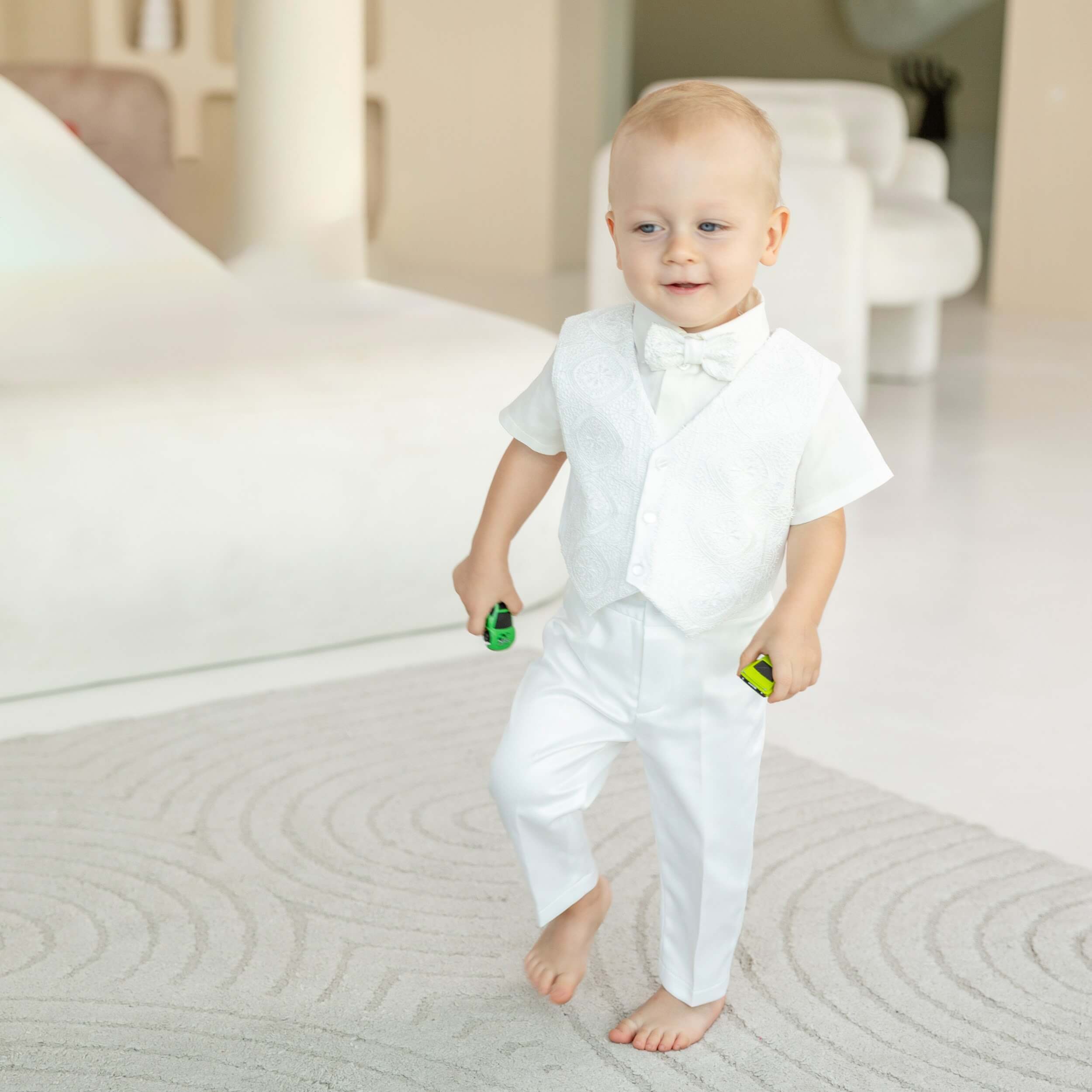 Child in a Baby Boy Baptism Suit  with a bow tie standing in a bright room.
