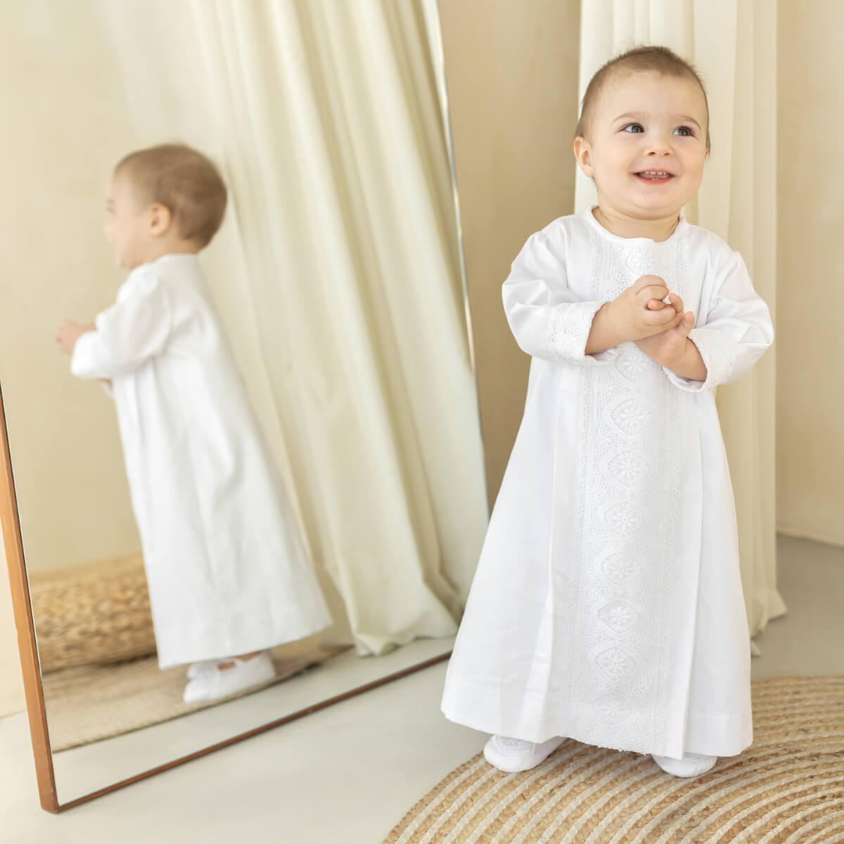 Baby in a Baptism Gown  standing in front of a mirror