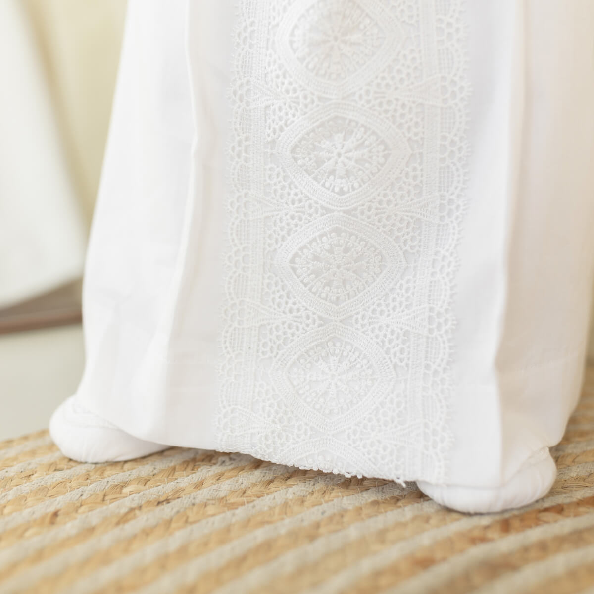 Close-up of a white fabric garment with delicate embroidered lace detailing, resting on a woven straw surface.
