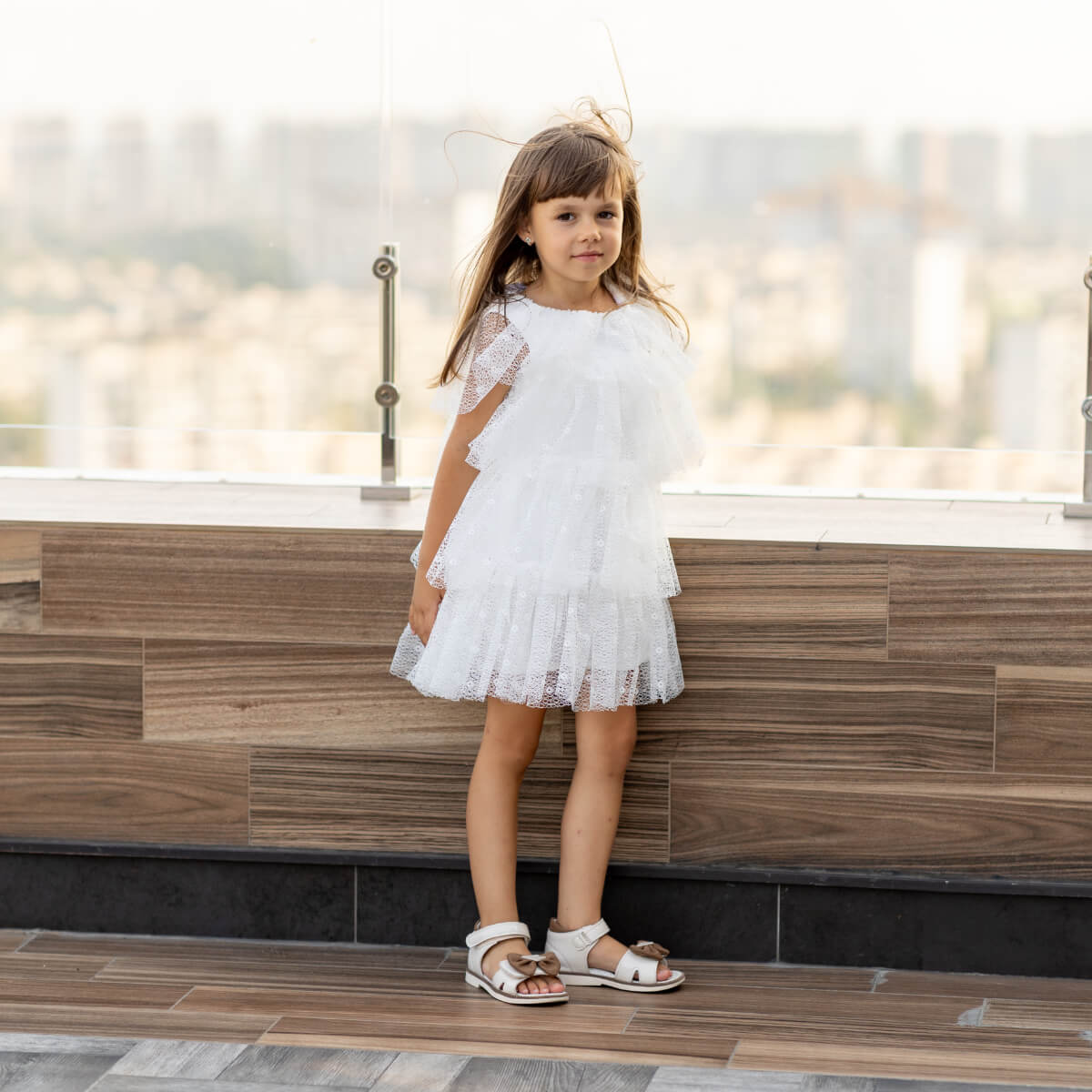 Young girl in a white dress standing on a wooden deck with a blurred background