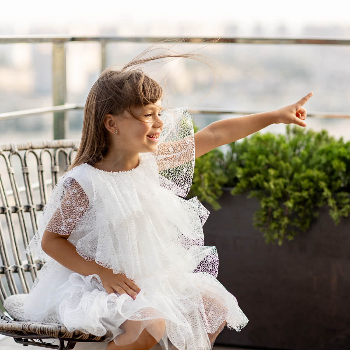 Young girl in a white dress sitting on a chair with a blurred background