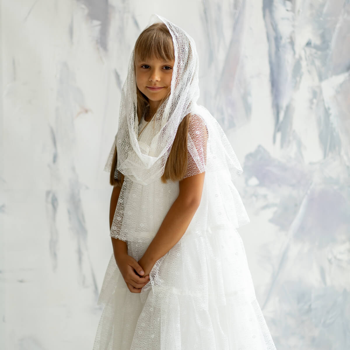 Young girl in Holy First Communion with a lace veil against a marble wall.