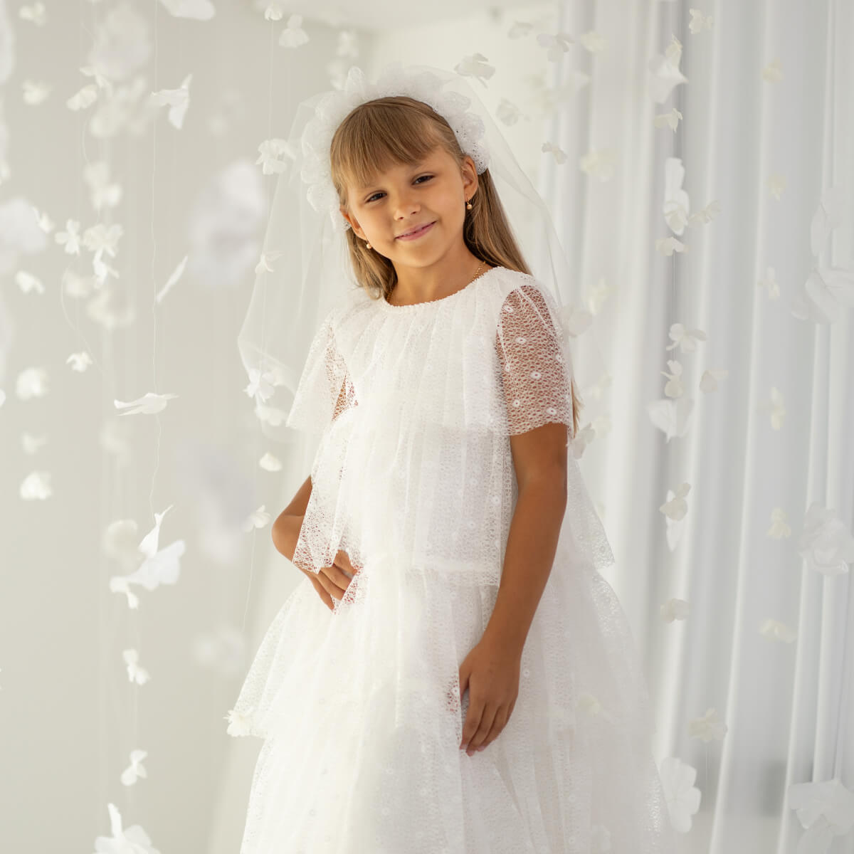 Young girl in Holy First Communion standing against a white floral backdrop