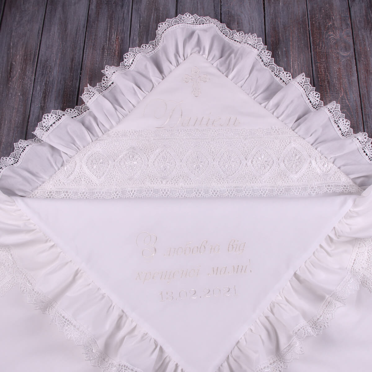 White embroidered chriatening blanket with lace trim on a wooden surface