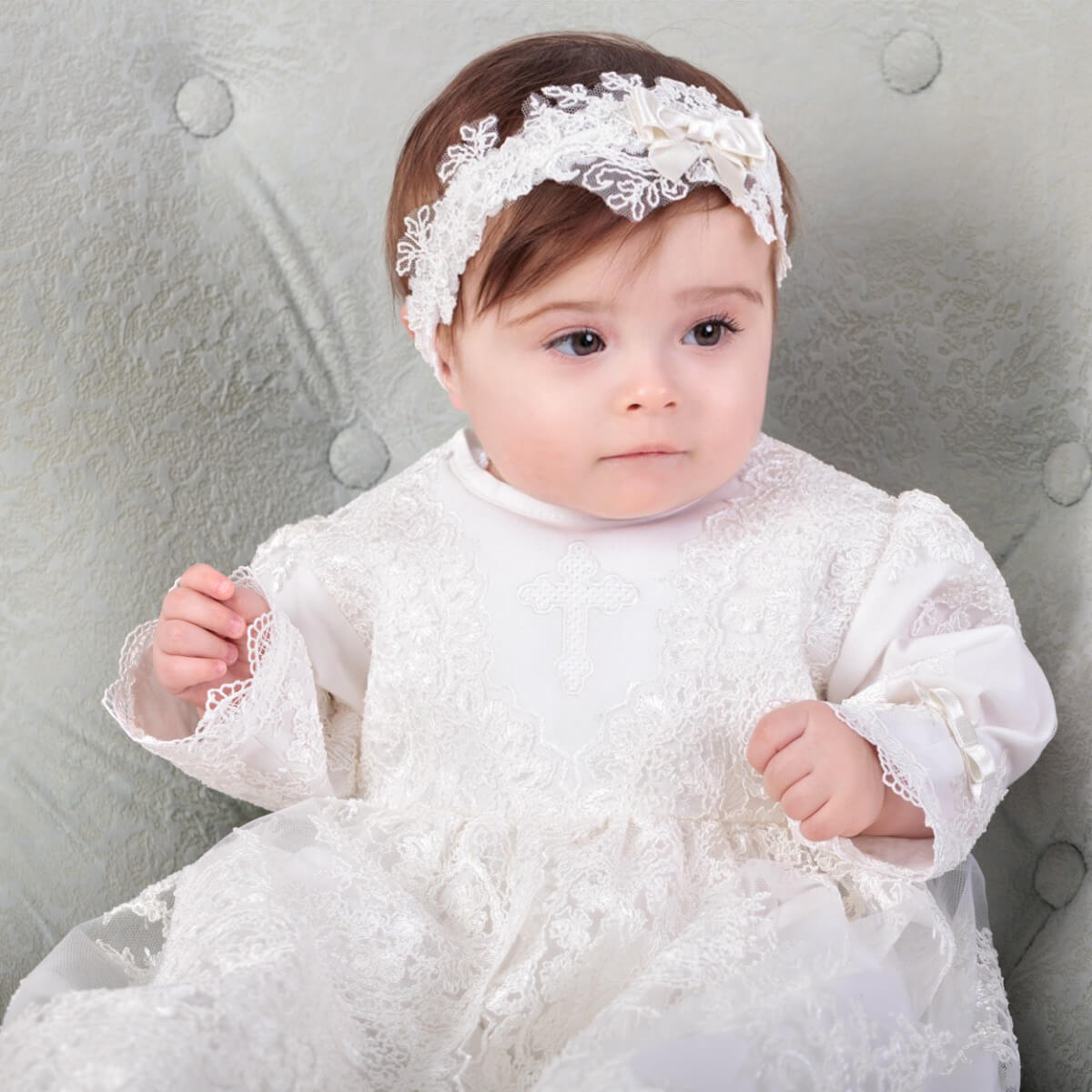Baby in a Heirloom Christening Gown for Girls with a matching headband, sitting on a gray cushion.