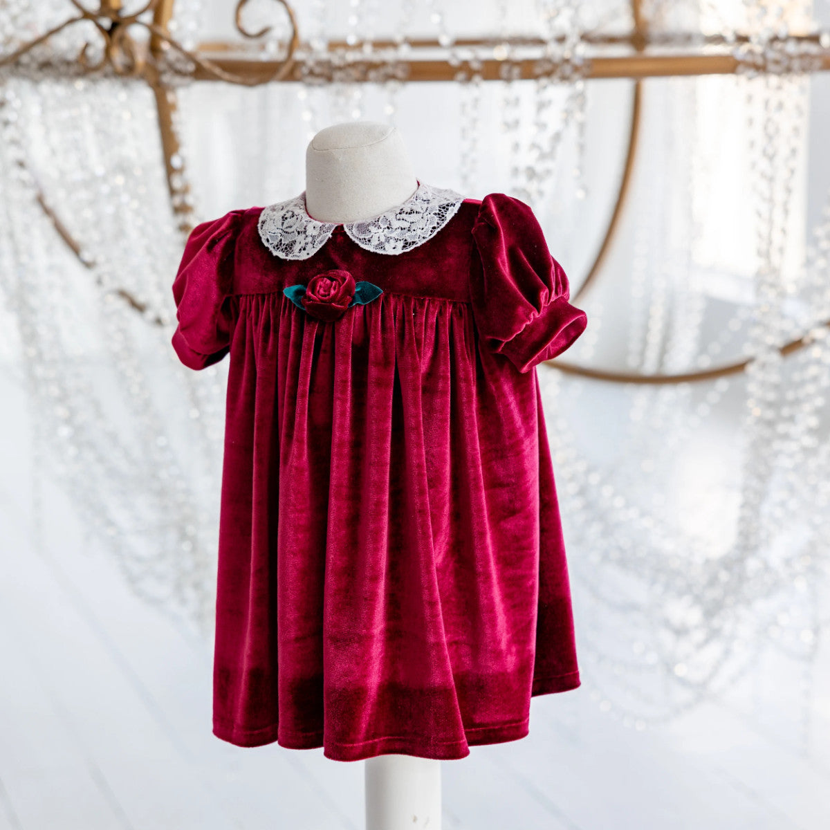 Red velvet dress with lace collar on a mannequin against a textured white background
