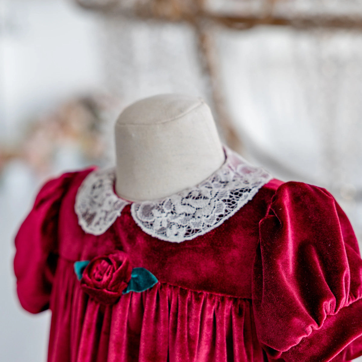 Red velvet dress with lace collar on a mannequin against a blurred natural background