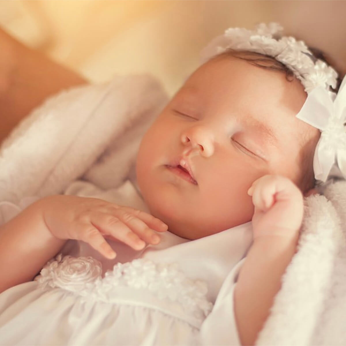 Sleeping girl in a white outfit wearing a matching baby headband.