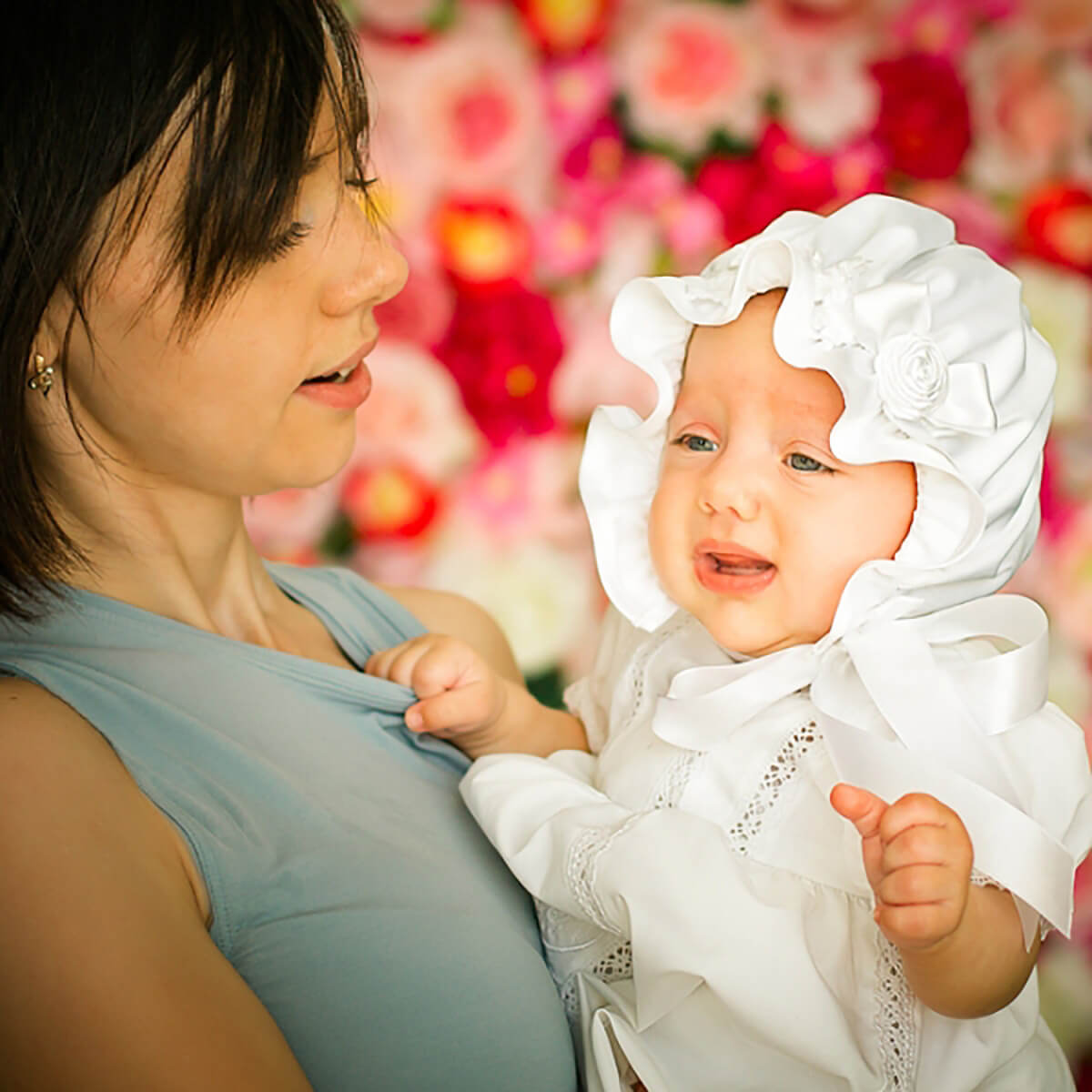 Woman holding a baby wearing a Silk Baptism Bonnet background