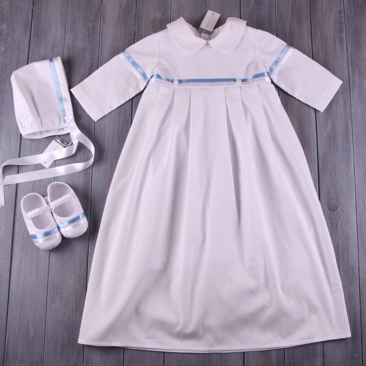 Christening outfit with blue trim, bonnet, and shoes on a wooden surface