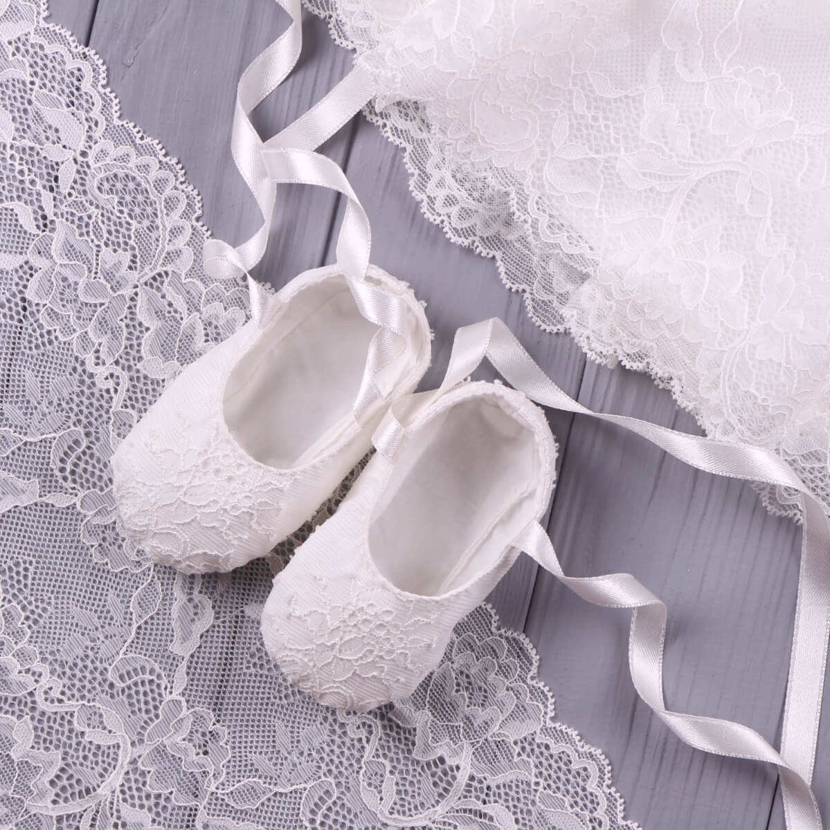  Christening Booties on a wooden surface with lace fabric and ribbons.