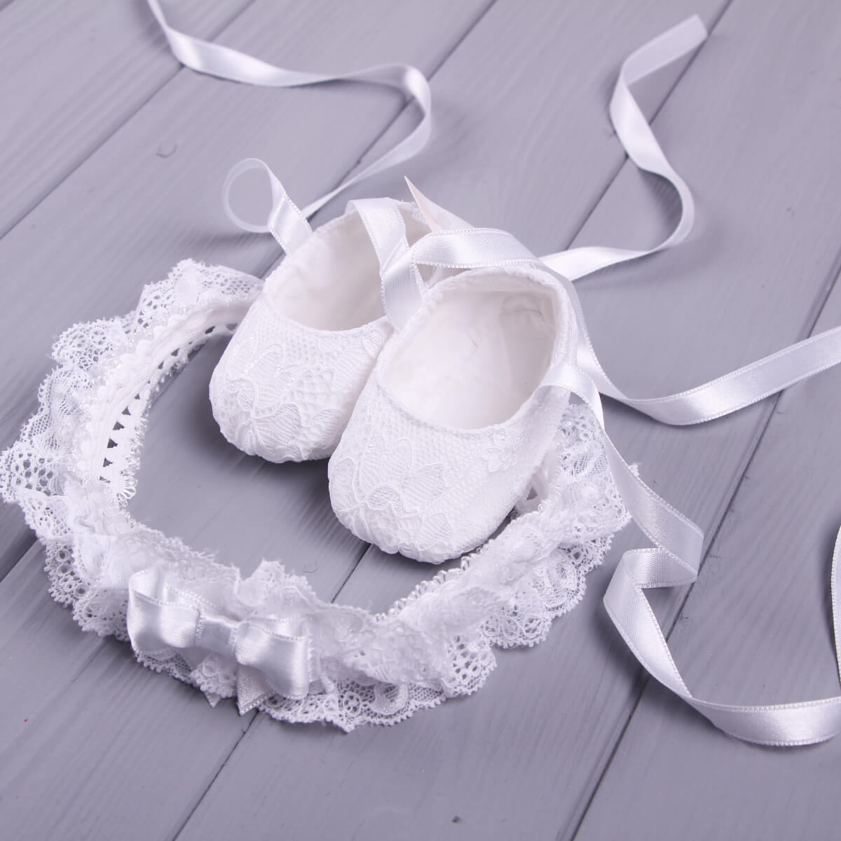  Christening Booties with lace and ribbons on a wooden surface