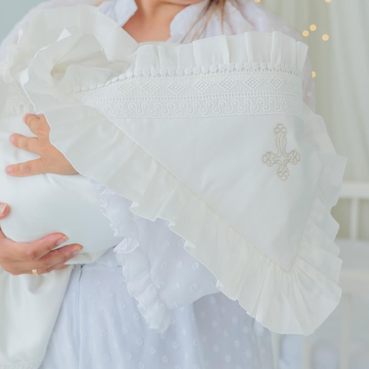 White baby outfit with smocked details and a cross emblem, held by a person.