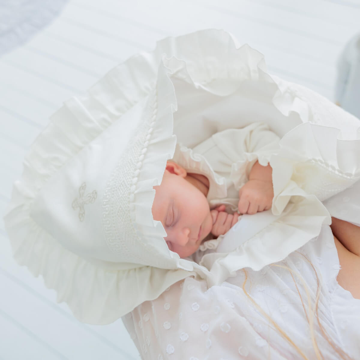 Baby wrapped in a white baptism blanket on a light blue background