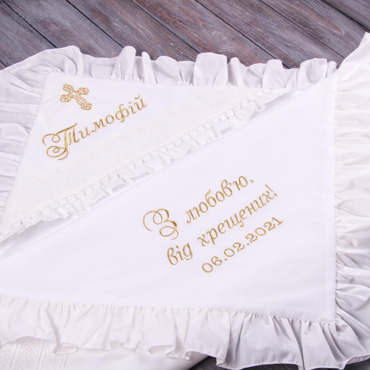 Ivory embroidered baptism blanket with gold text on a wooden surface