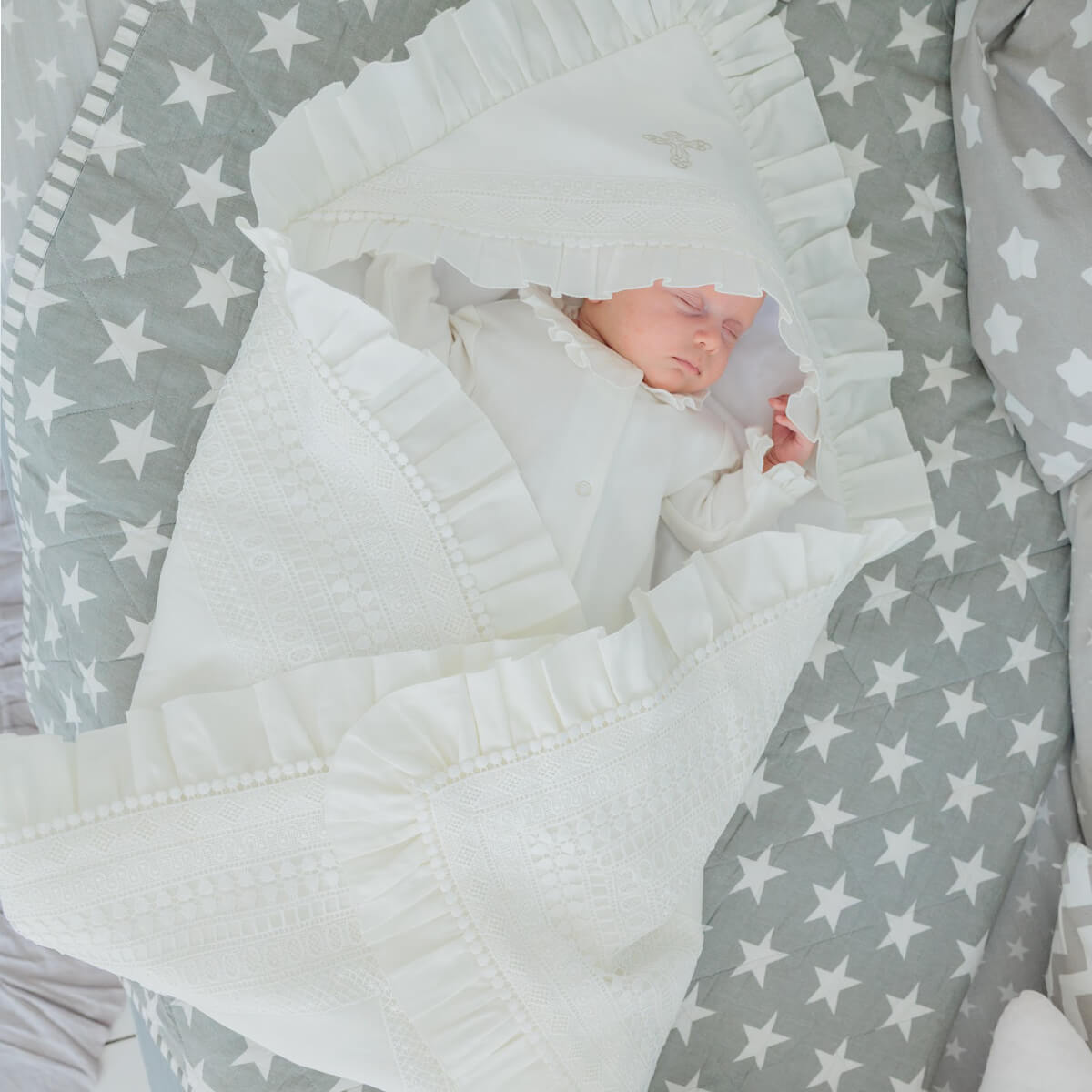 Baby wrapped in a white blanket with star pattern on gray background