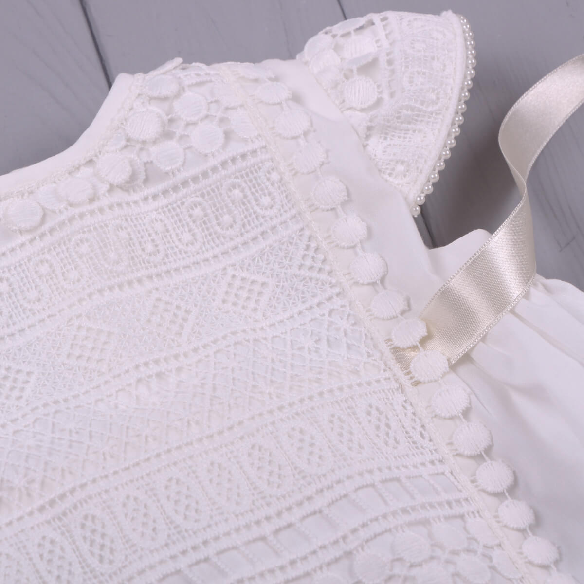 Close-up of a Baptism Dress with Macramé Lace with a ribbon on a gray background