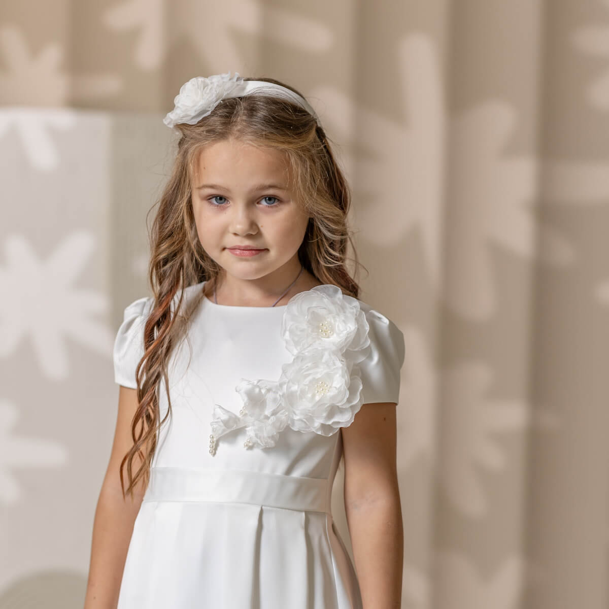 Young girl in a Simple Communion Dress with floral details against a neutral background