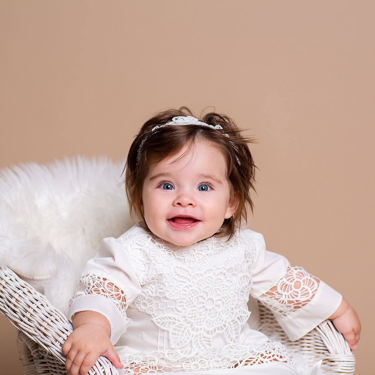 Baby in a  Baptism Gown for Baby Girl sitting on a white chair against a beige background
