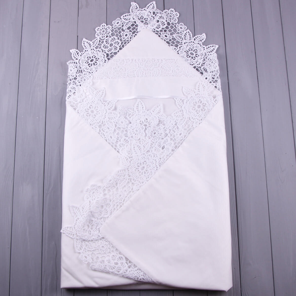 White lace-trimmed christening blanket on a wooden surface