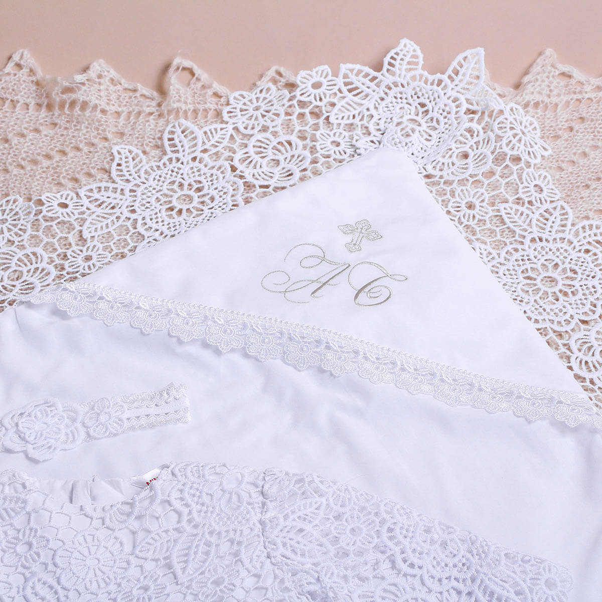 White lace-trimmed christening blanket with monogram on a beige background