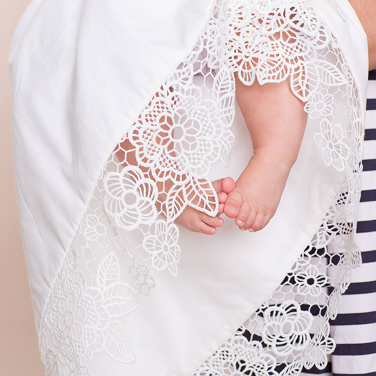 Close-up of a baby's feet in a white lace christening blanket with a striped garment partially visible.